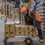 Operatore di magazzino che carica le merci su carrelli a mano e carrelli a mano