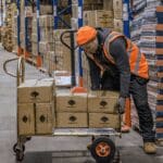 Operatore di magazzino che carica le merci su carrelli a mano e carrelli a mano
