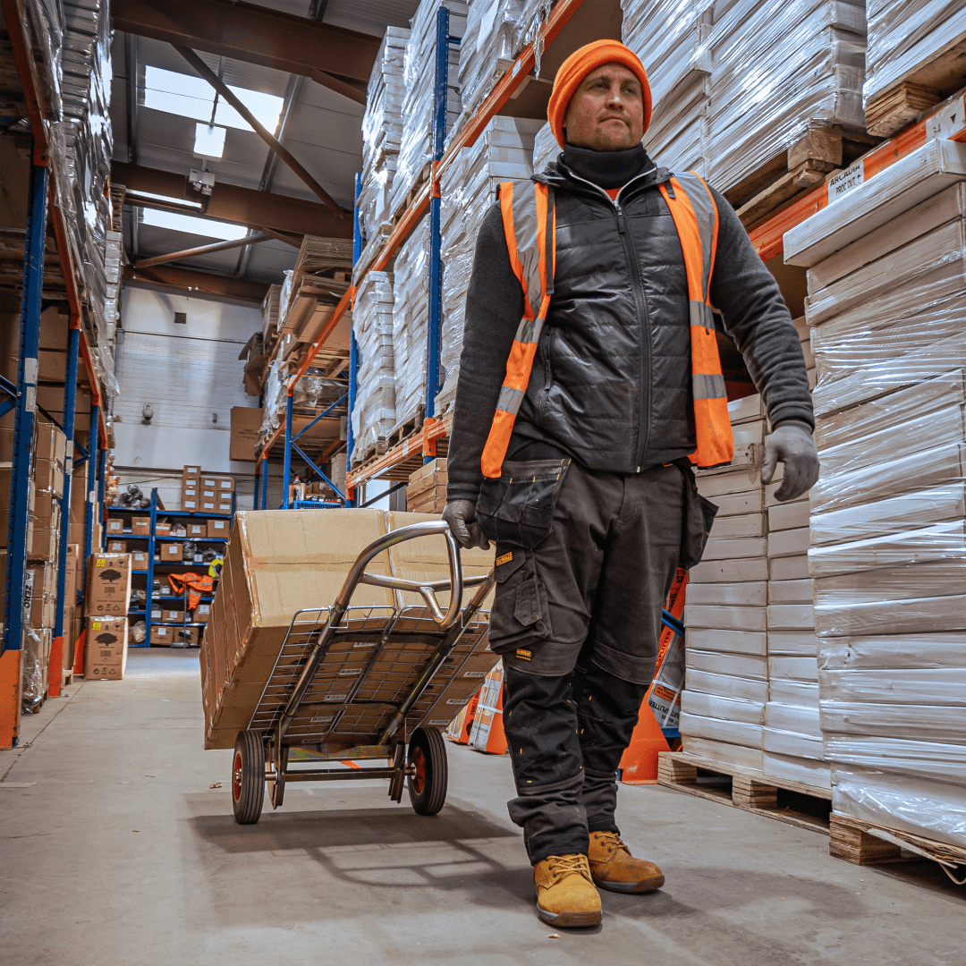 Opérateur d'entrepôt transportant des marchandises avec un chariot à main et une brouette.