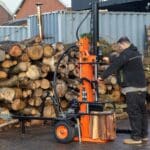 a machine with a wheel and wheels in front of a pile of logs